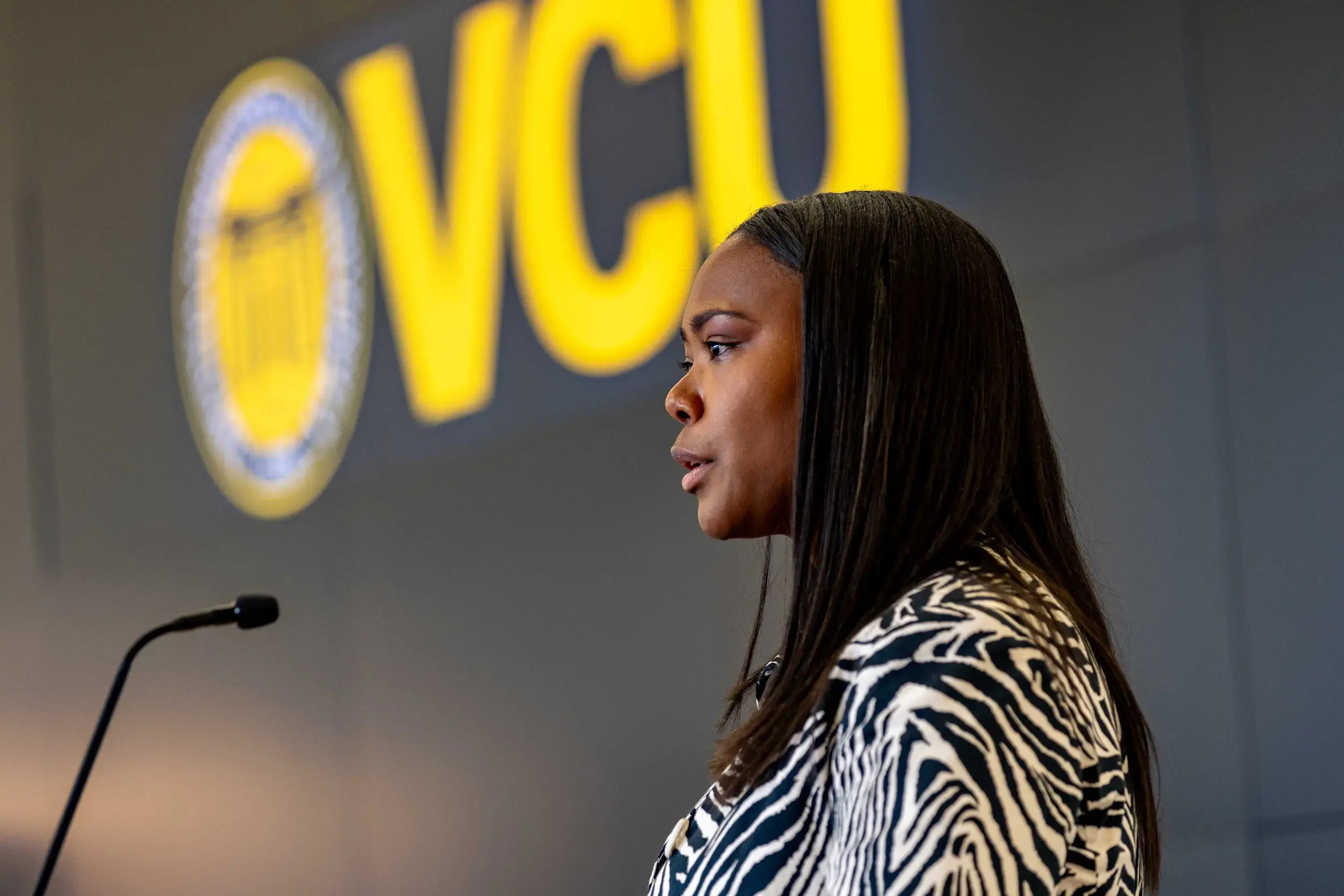 Chelsea Gary from the shoulders up. She is speaking behind a microphone and behind her on the wall are yellow letters that spell out VCU