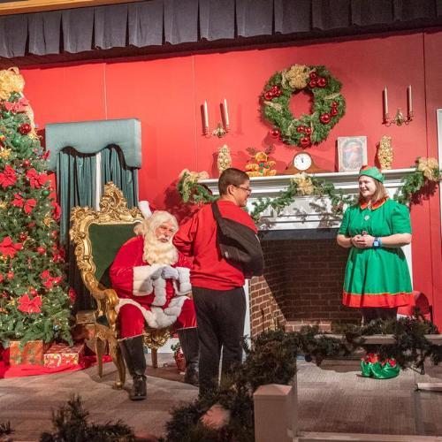 Between a Christmas tree and fireplace, Santa and his elves greet a child at the Children's Museum