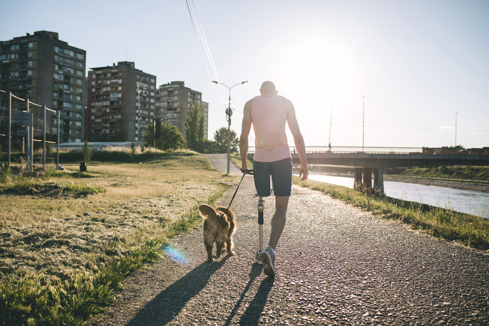 Man with a prosthetic leg walking his dog down a path