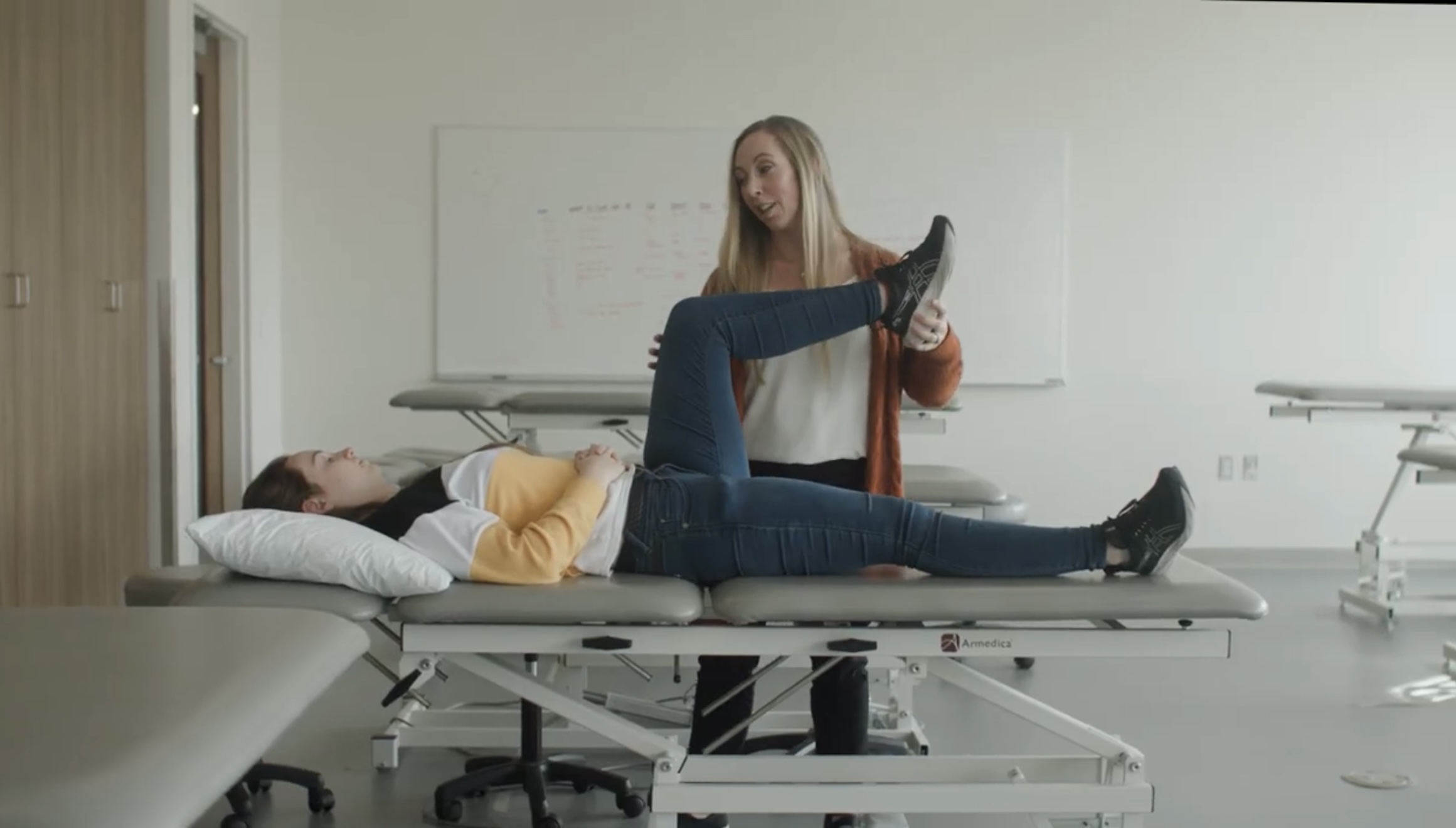 Feather Wright performing physical therapy exam by lifting participants leg and bending at knee