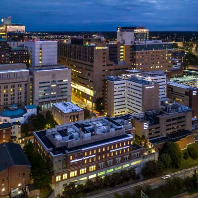 Aerial view of the V.C.U. Health campus at dusk with multiple illuminated buildings, including the V.C.U. Massey Cancer Center and surrounding city lights